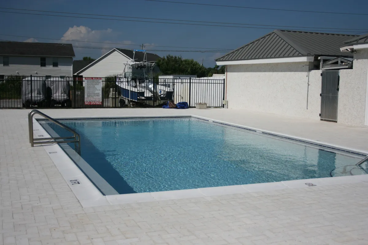 A serene exterior shot of a swimming pool with a surrounding deck, featuring a boat moored in the background. The image evokes a leisurely atmosphere, suggesting relaxation by the water and easy access to aquatic adventures.