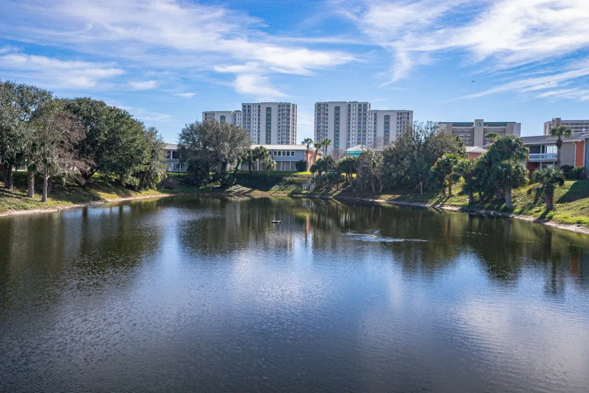 A serene view of Turtle Lake, with its reflective water surface framed by lush greenery, palm trees, and distant condo buildings. The tranquil setting is ideal for lakeside strolls, relaxation, or simply soaking up nature’s beauty, all within the secure boundaries of the community.